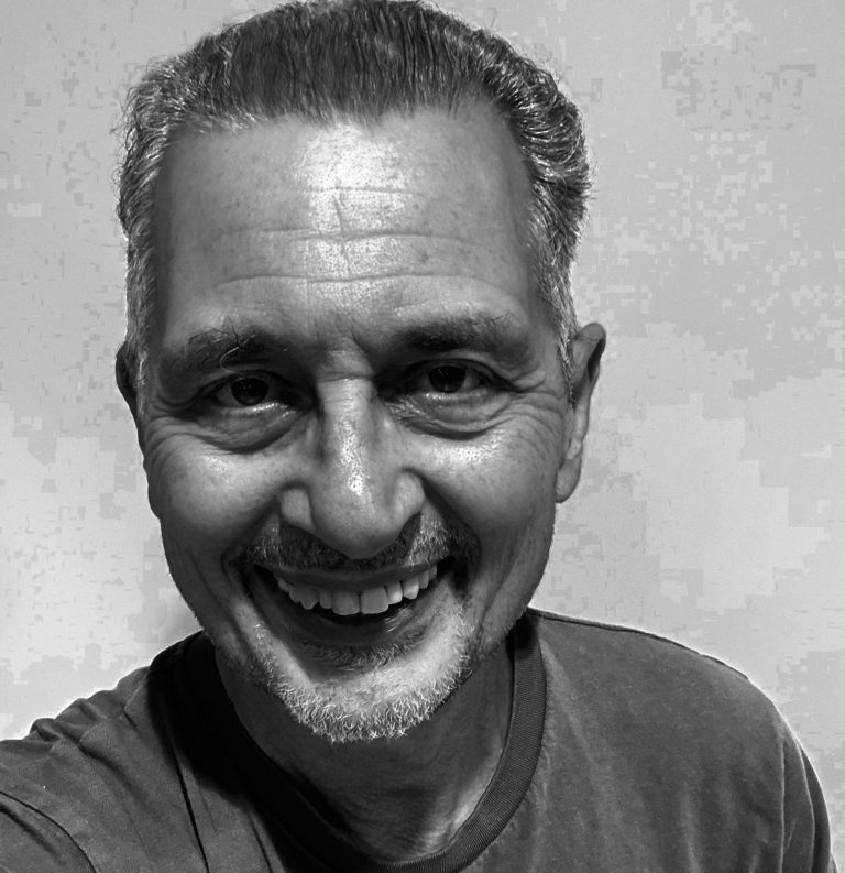 Denis Taylor Smiling man with short grey hair and a light beard, wearing a t-shirt.
